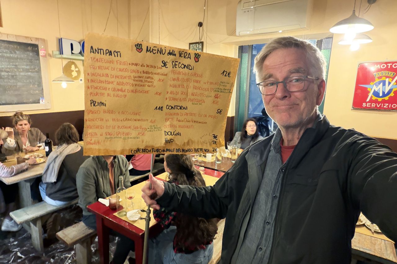 Rick Steves holding a menu in what appears to be a local restaurant setting