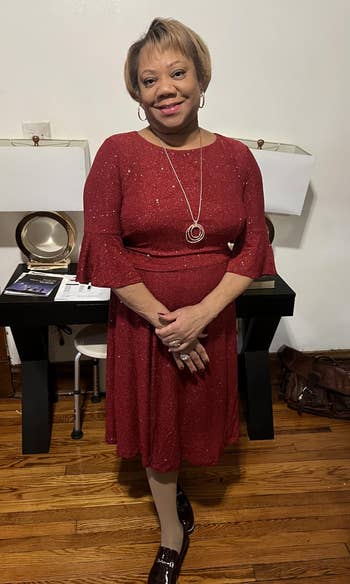Person in an elegant, sparkly dress stands smiling in a stylish interior, featuring a modern console table and decorative items