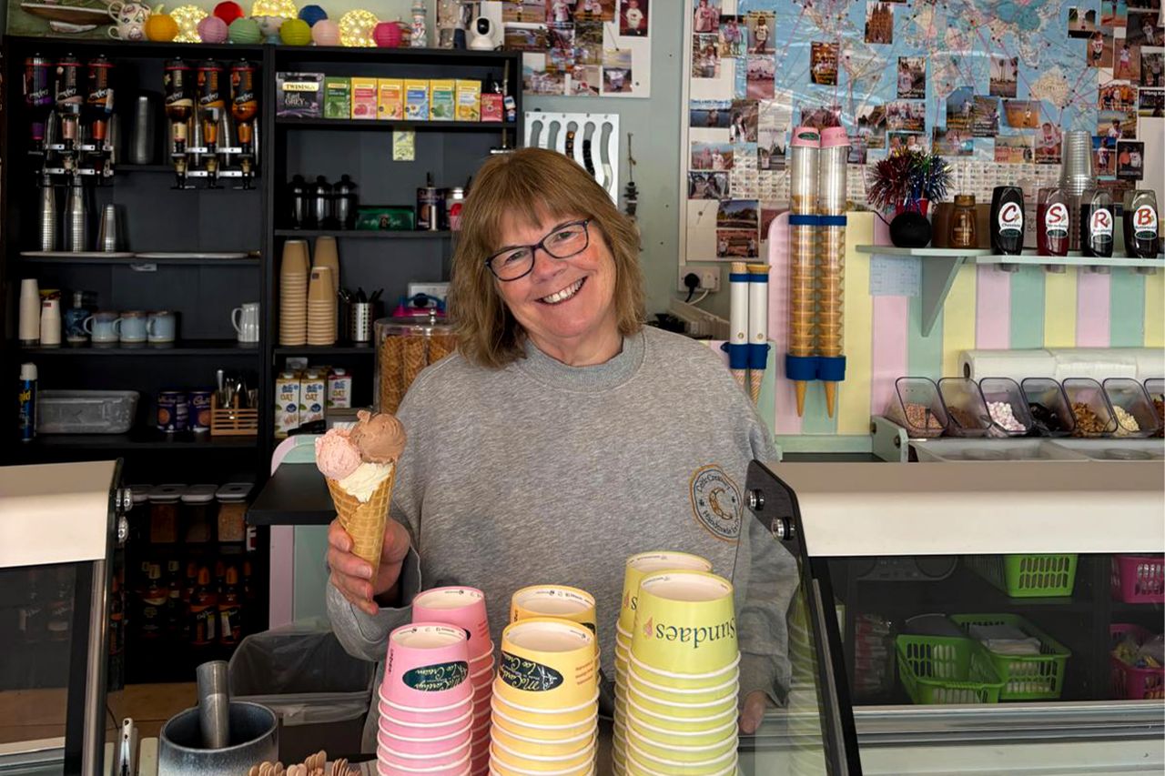 A woman standing behind an ice cream counter holding a cone