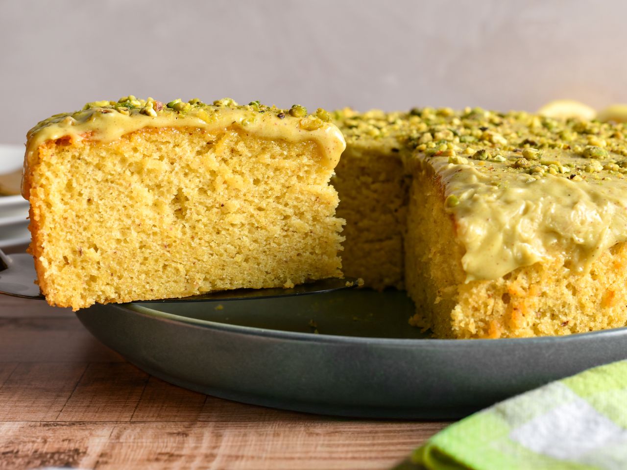 round pistachio lemon cake with 1 slice on spatula on dark grey plate