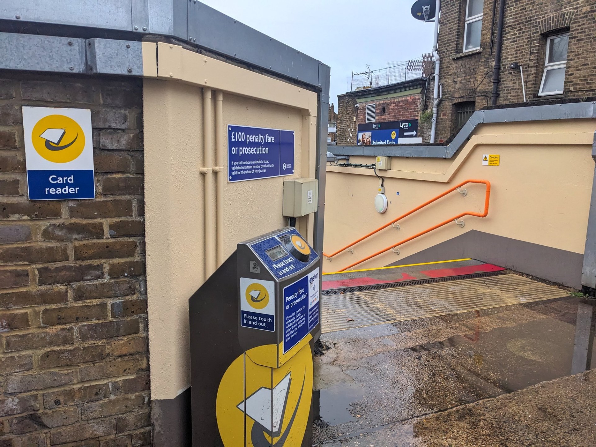 A yellow contactless card reader for public transport payment stands at the entrance to Stoke Newington station with a stairway leading down to the platforms
