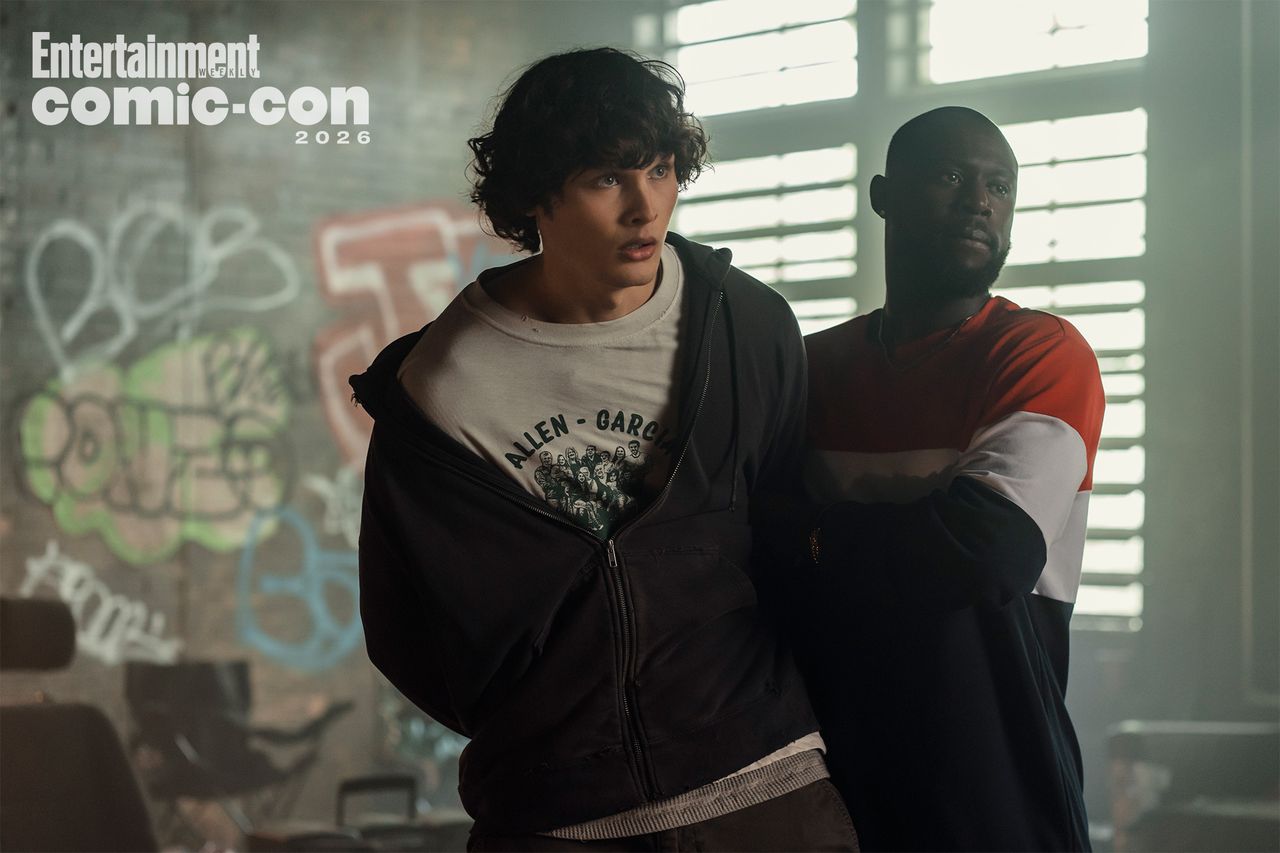Two individuals standing in a dimly lit room with graffiti on the walls one looking to the side and the other slightly behind