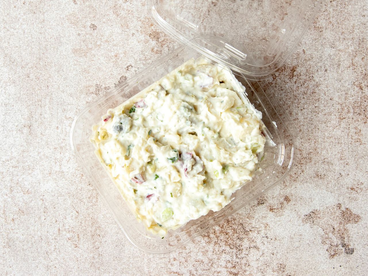 Container of prepared potato salad with visible chopped ingredients in a clear plastic box