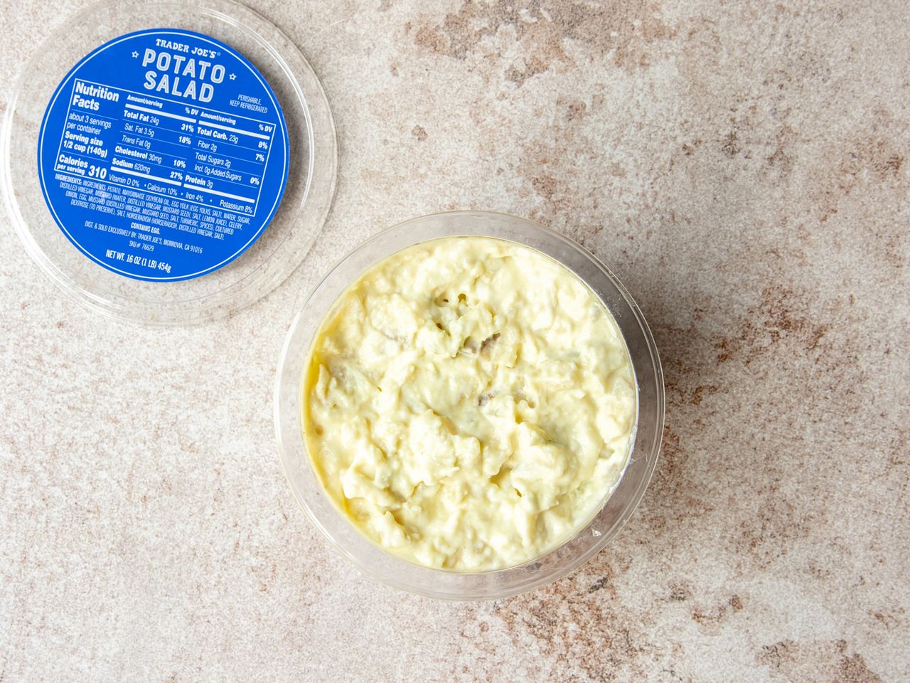 A container of Trader Joes potato salad with the lid placed nearby displaying nutritional information