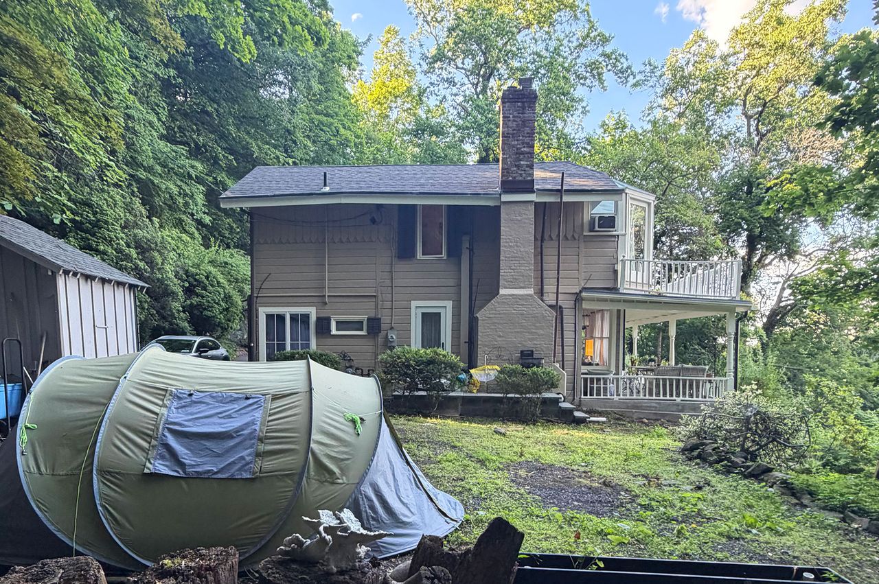 Back view of a twostory house in a wooded area with a tent set up on the lawn