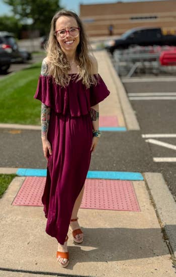 Person walking in a parking lot, wearing a flowing off-shoulder dress with a ruffled neckline and sandals, smiling