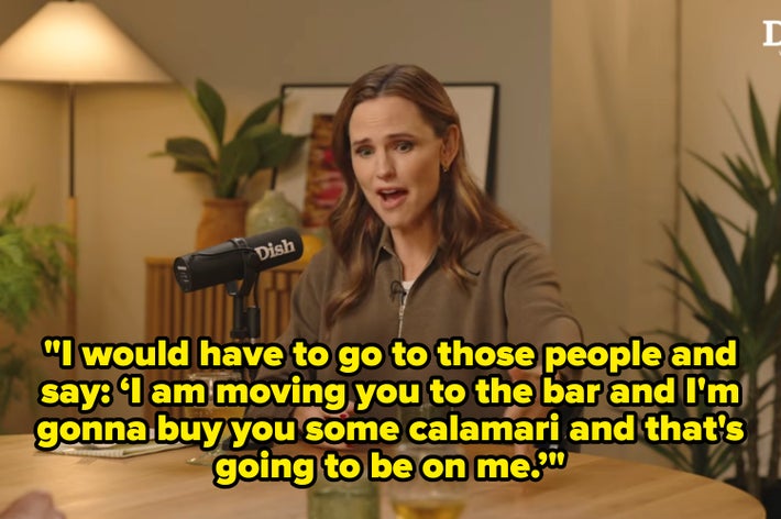 Person at a podcast table, gesturing expressively while speaking into a microphone labeled "Dish," with a casual, relaxed setting and plants around