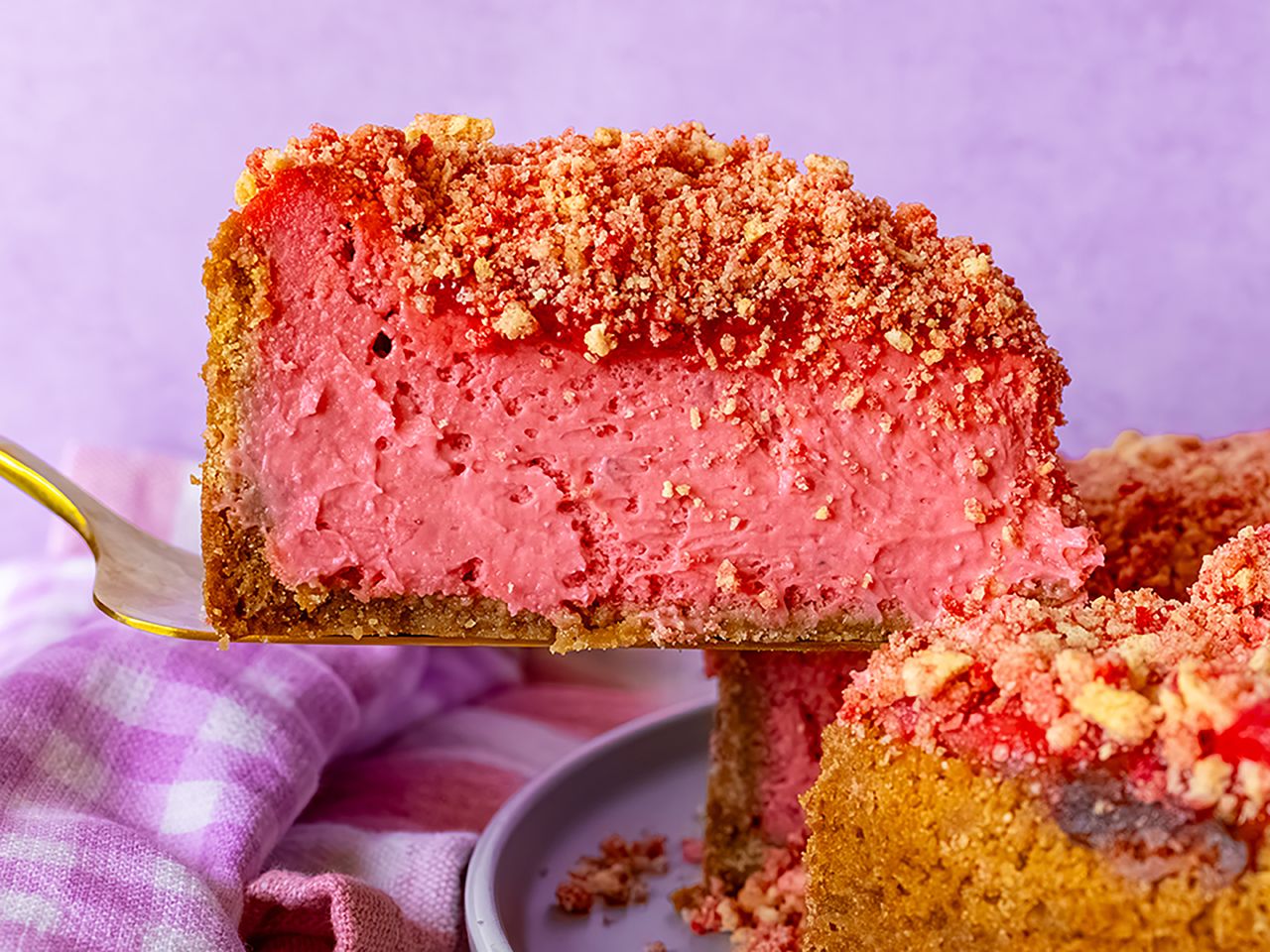 slice of strawberry crunch cheesecake on spatula being lifted from the full cheesecake