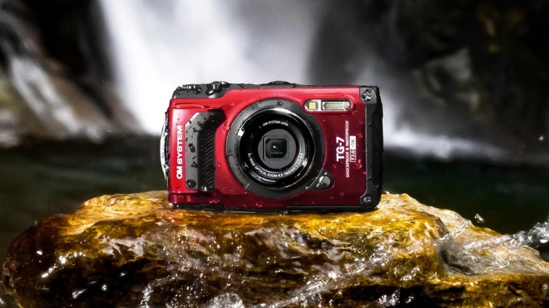The OM System Tough TG-7 on a rock with water splashing around it with a waterfall in the background