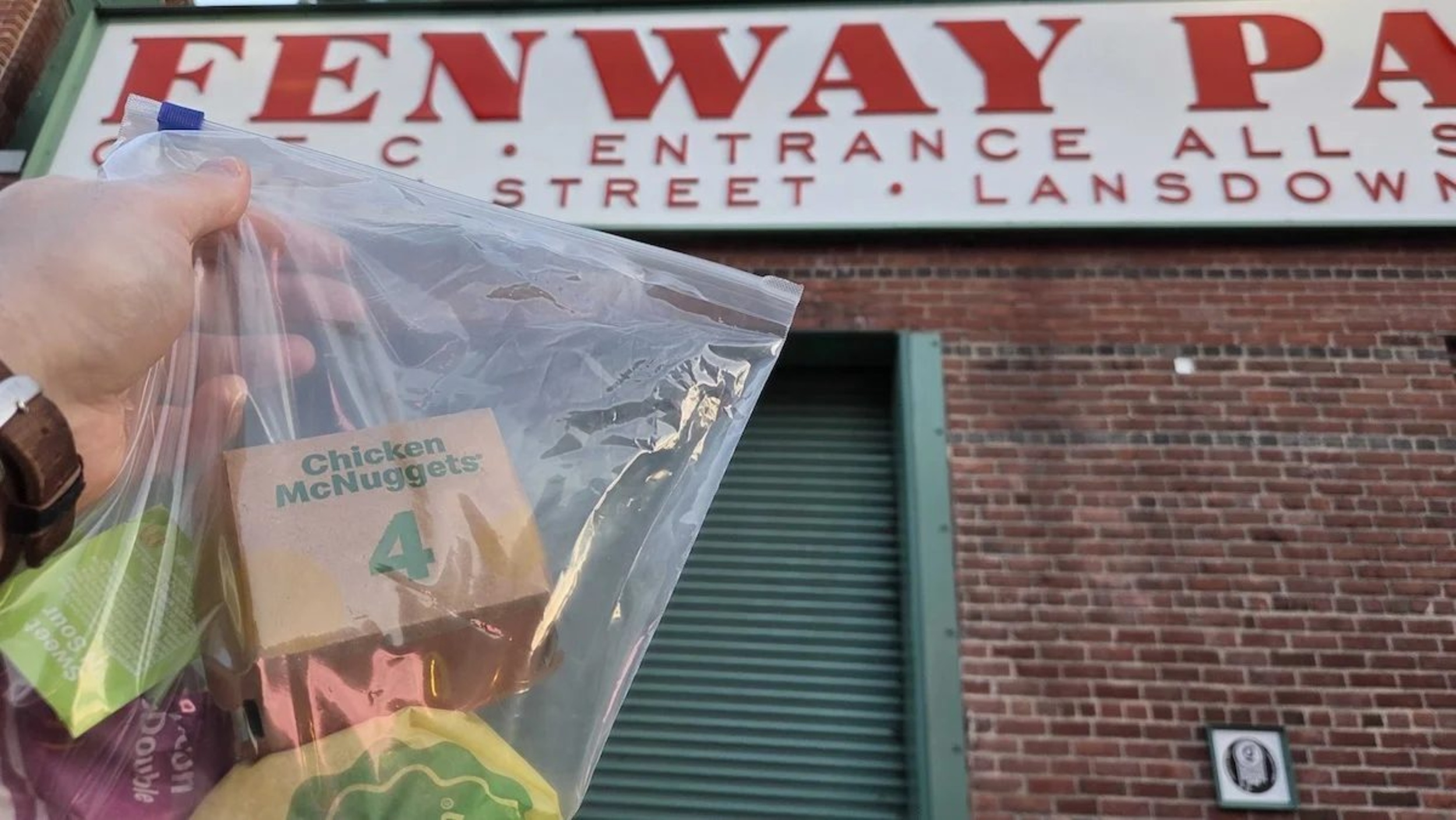 A clear bag of McDonald's food held up near a Fenway park sign