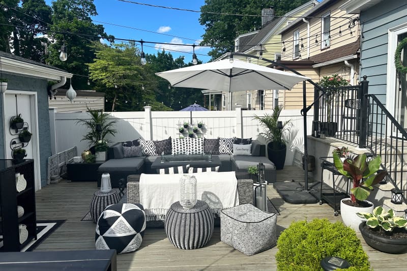 Gray couch and black, white, and gray accessories in renovated backyard with white umbrella.