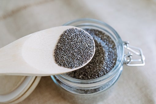 Poppy seeds on a wooden spoon over a glass jar
