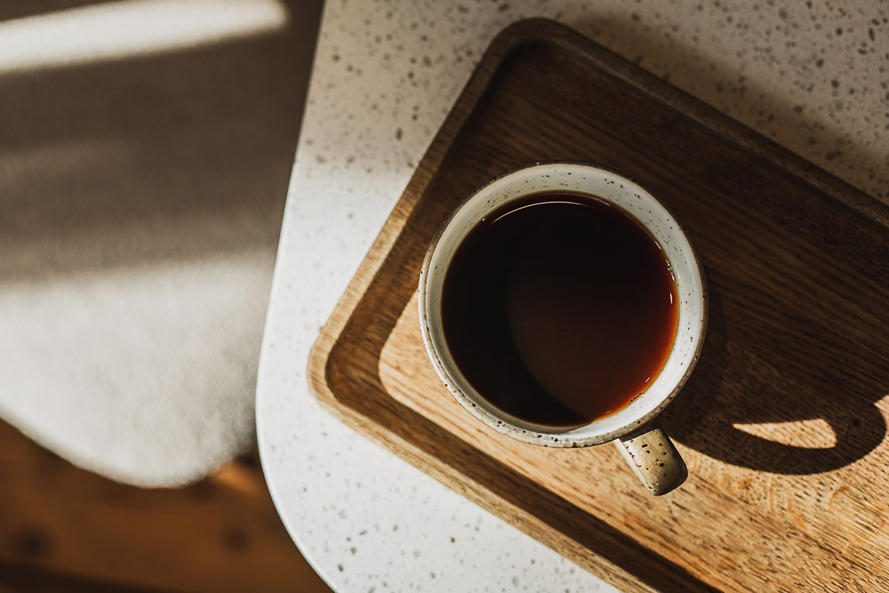 Cafe culture, long black or filter coffee. Cup with hot beverage in sunshine, majestic light and shadows on table. No people, copy space background.