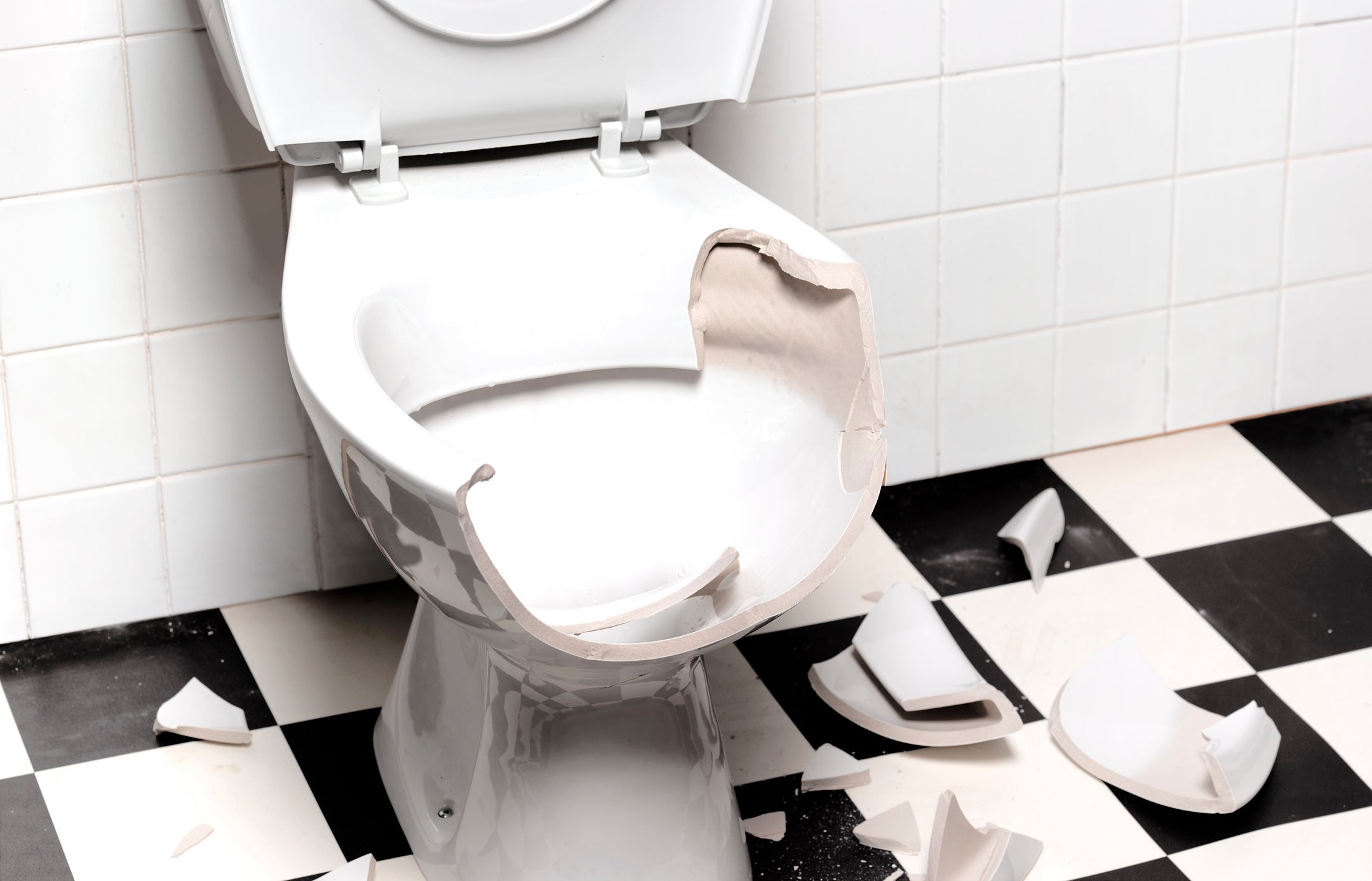 Broken toilet with shattered pieces on tiled floor