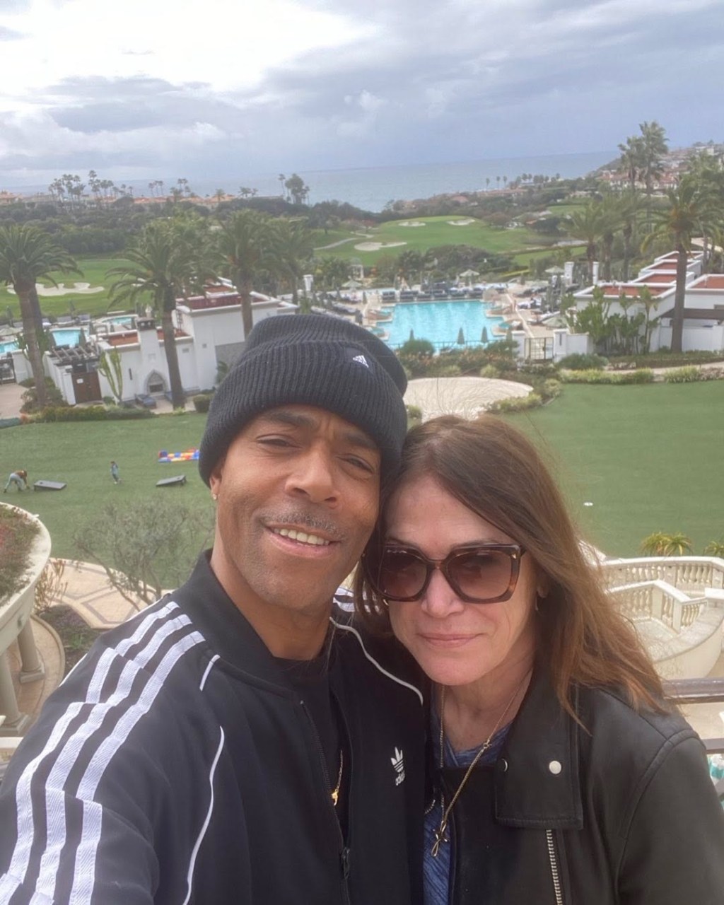 Kim Delaney and James Morgan taking a selfie with a resort and ocean in the background.