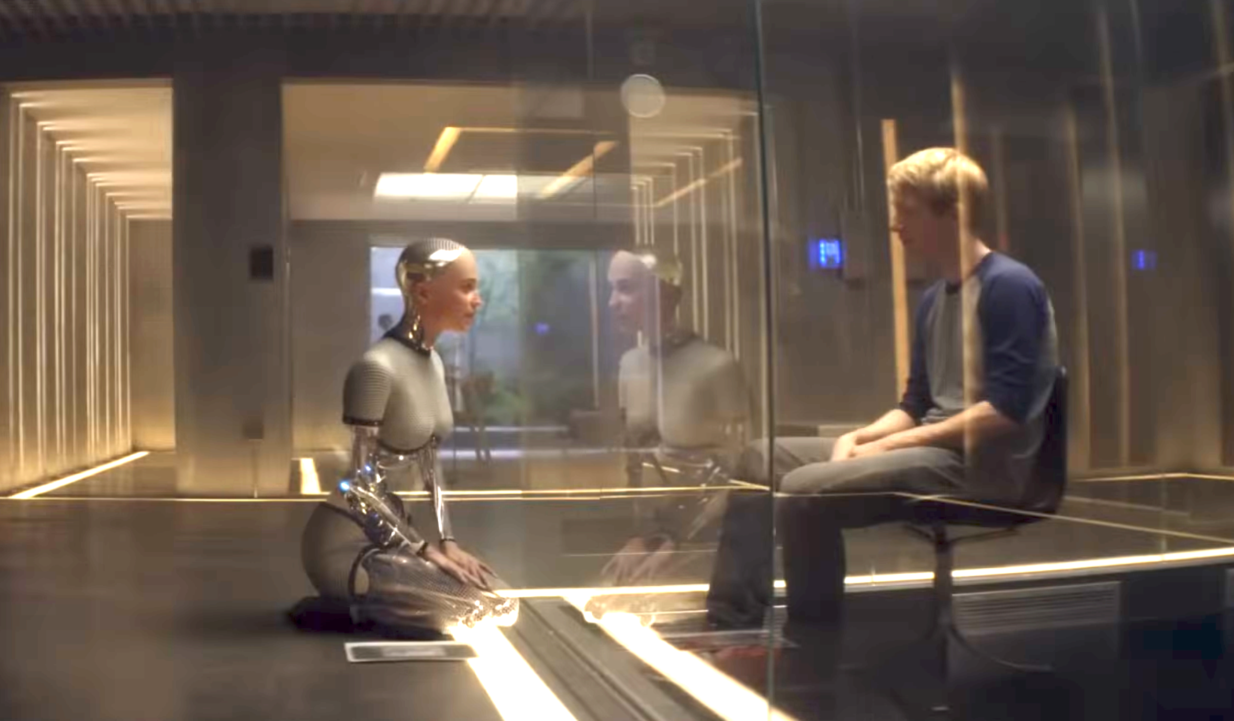 A humanoid robot and a person sit face-to-face separated by glass in a modern, futuristic room