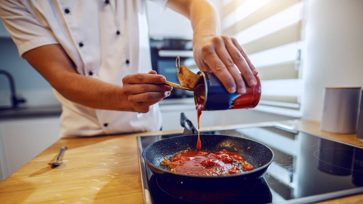 close-up-of-creative-experienced-caucasian-chef-in-uniform-adding-peeled-tomato-domestic-kitchen-interior