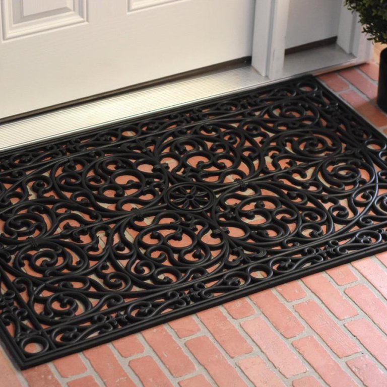 The Fleur De Lis Living Nonslip Outdoor Doormat in place on a brick patio outside a front door