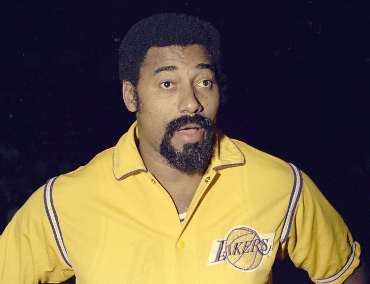 Wilt Chamberlain stands with his mouth open while wearing a gold Lakers warmup jacket