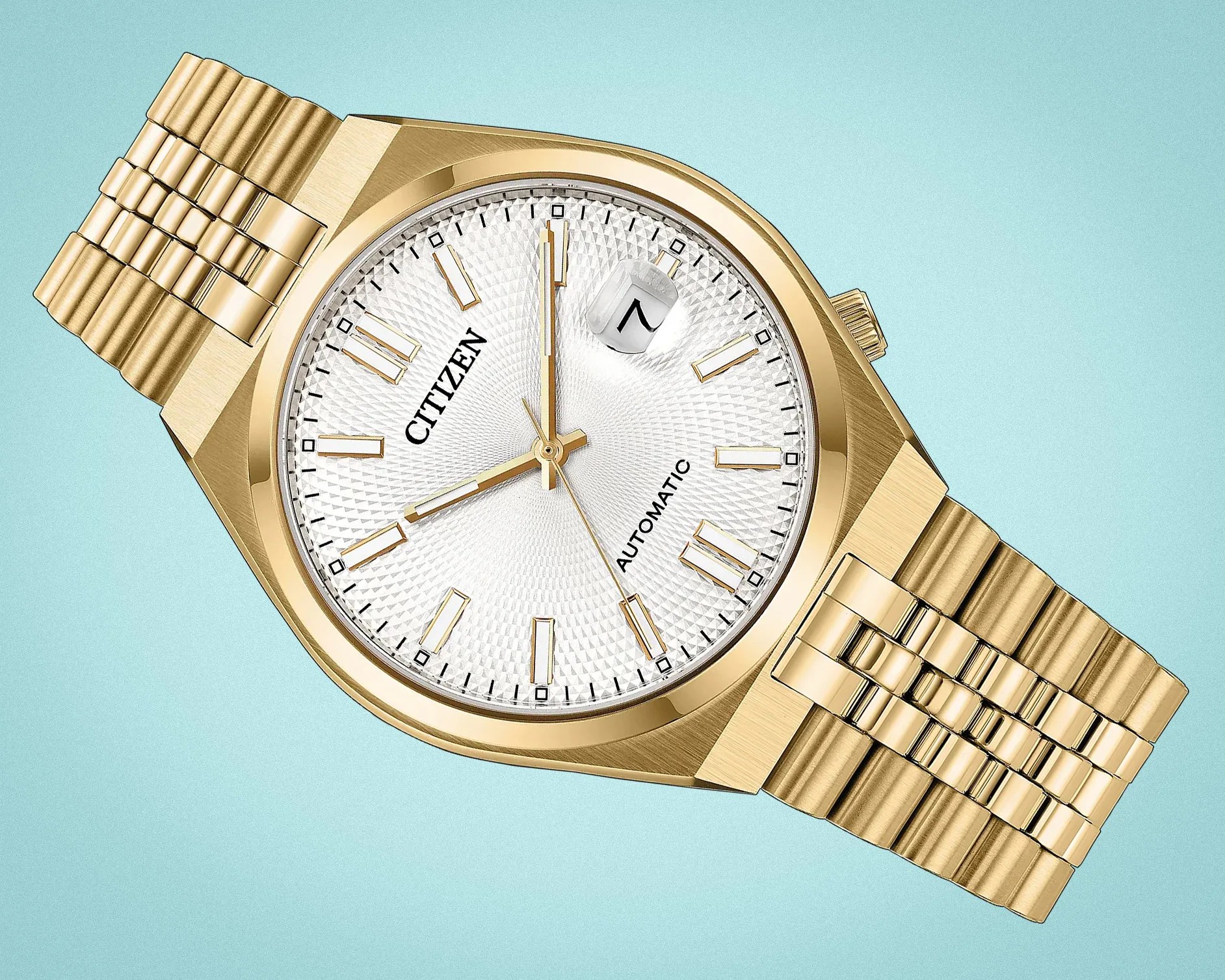 Gold Citizen automatic wristwatch with textured white dial and date magnifier on a light blue background.