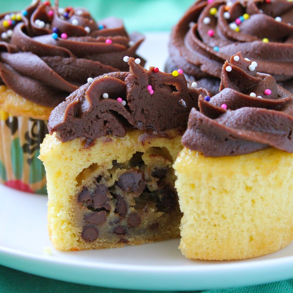 close up view of vanilla cupcakes with cookie dough filling with chocolate icing and rainbow sprinkles on a white platter