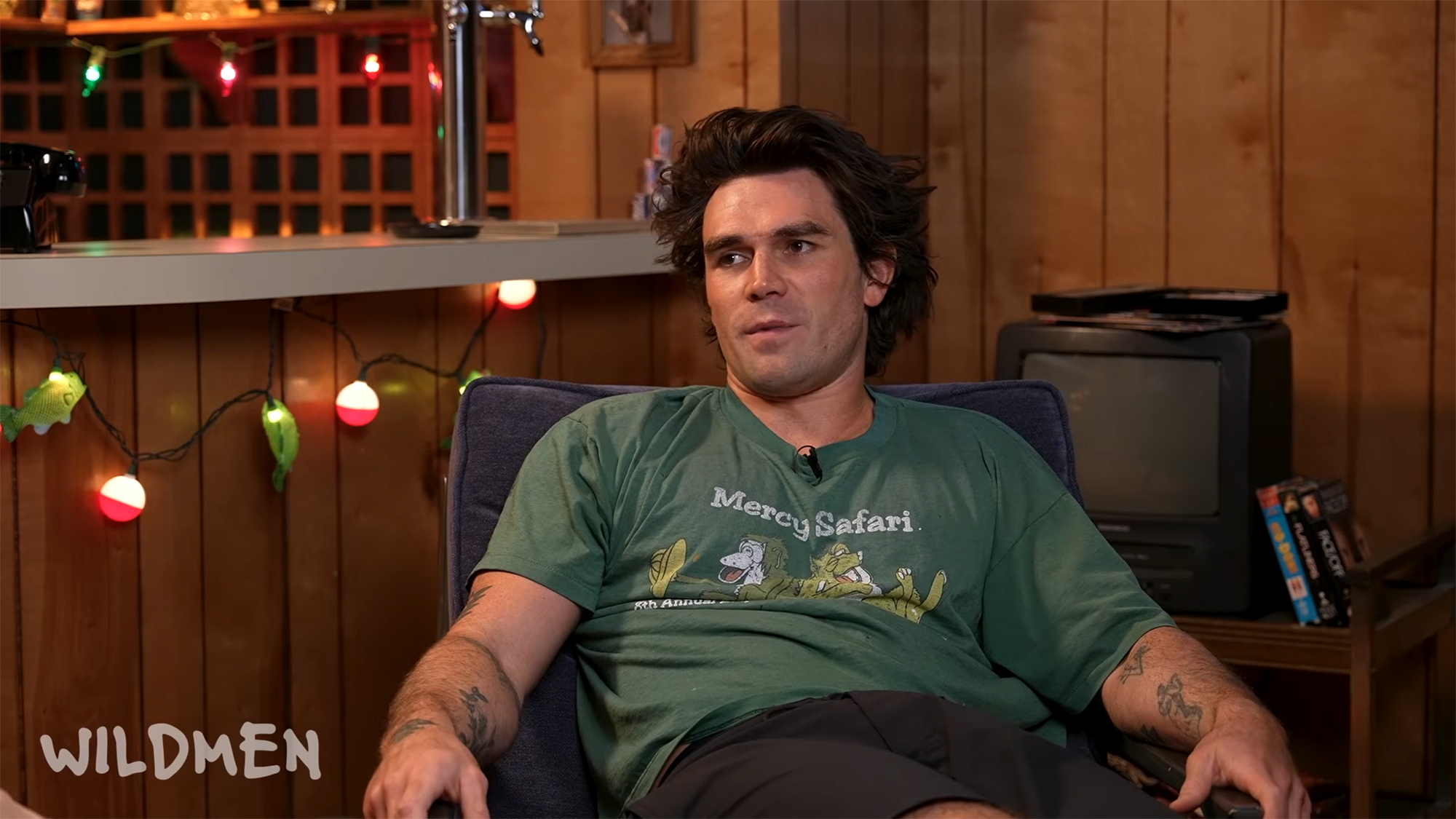 KJ Apa sitting on a dark blue chair while being interviewed on the Wildmen podcast.