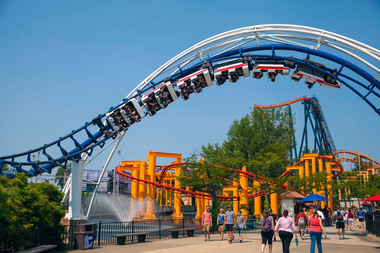 A roller coaster ride with people onboard at Cedar Point amusement park surrounded by additional visible rides and parkgoers walking below