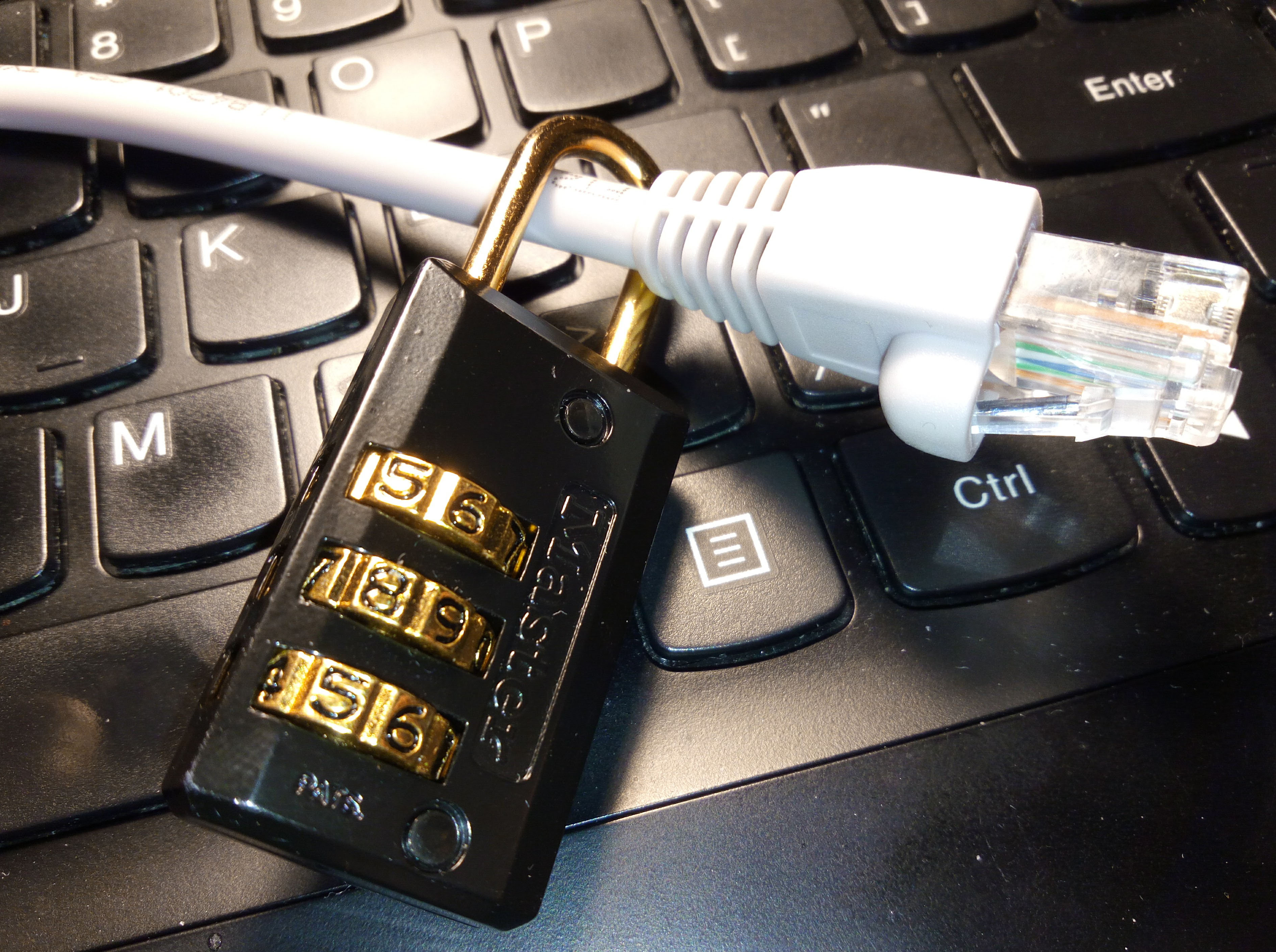 A combination lock wrapped around an ethernet cable. Both are resting a top a laptop keyboard.