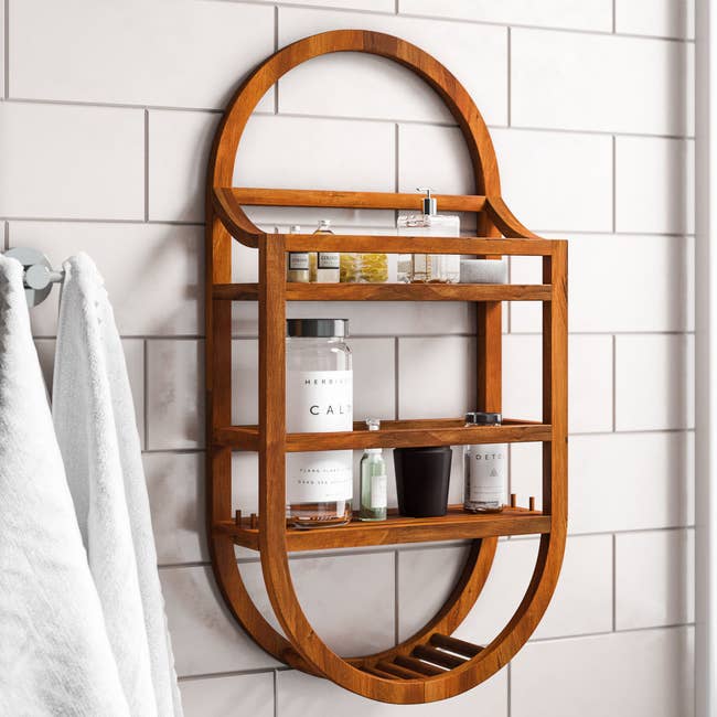 Wooden shower caddy mounted on tiled wall, holding toiletries and a towel on a nearby hook. Stylish bathroom storage solution