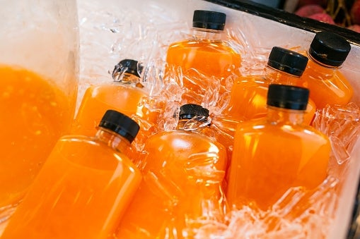 Bottles of orange juice are chilled on ice inside a cooler