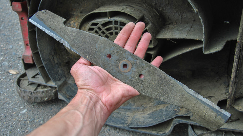 A man's hand holding a lawn mower blade