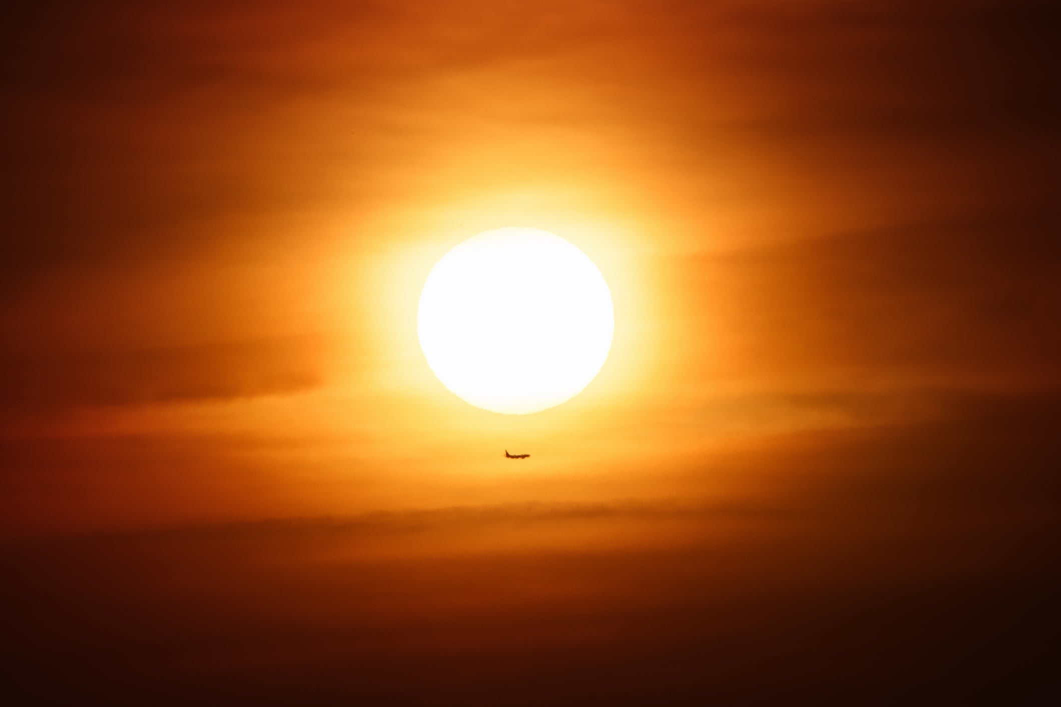 A small airplane silhouetted against a large setting sun in a cloudy sky