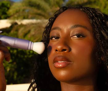 Person applying makeup with a brush applicator in an outdoor setting