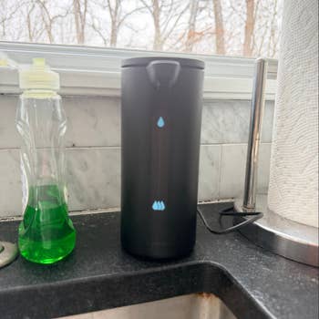 Automatic soap dispenser on a kitchen counter near a dish soap bottle and paper towel holder