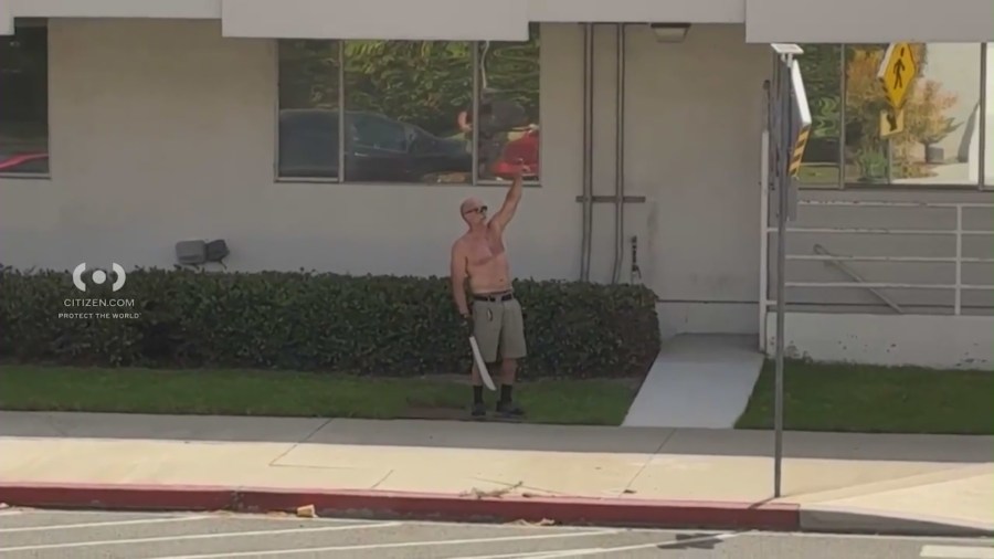 Police officers surround a commercial building as a shirtless man holding a machete is seen during a standoff that ended in an officer-involved shooting