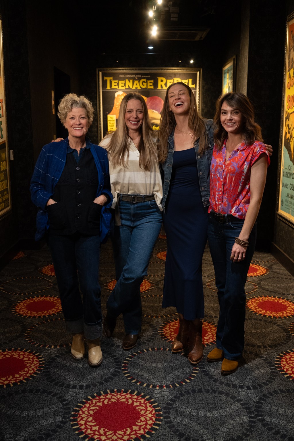 Four smiling women, including Adrianne Palicki and Aimee Teegarden, posing in a hallway with movie posters.