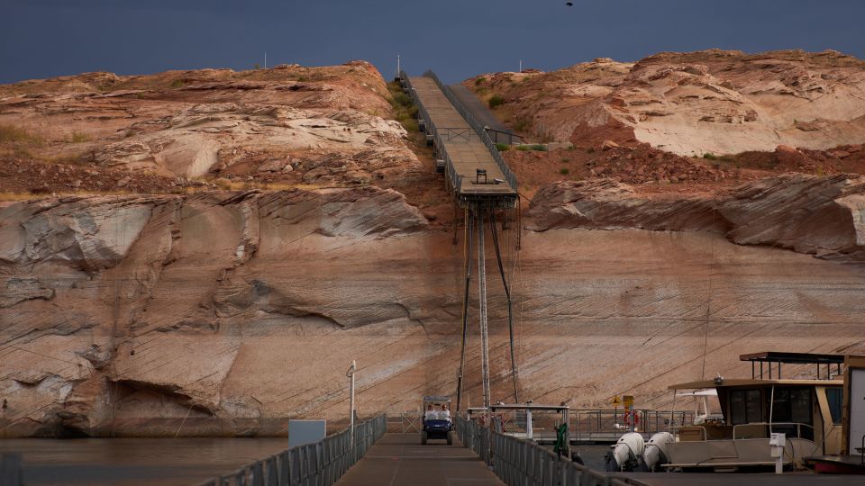 People ride a golf cart beneath a protruding dock used during higher water levels at the Antelope Point Marina on Lake Powell, July 14, 2026, near Page, Arizona. - John Locher/AP