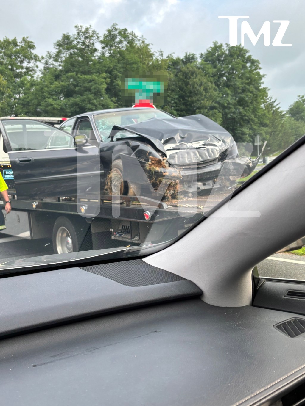 A severely damaged black car, with its front end crushed and windshield shattered, is loaded onto a tow truck.