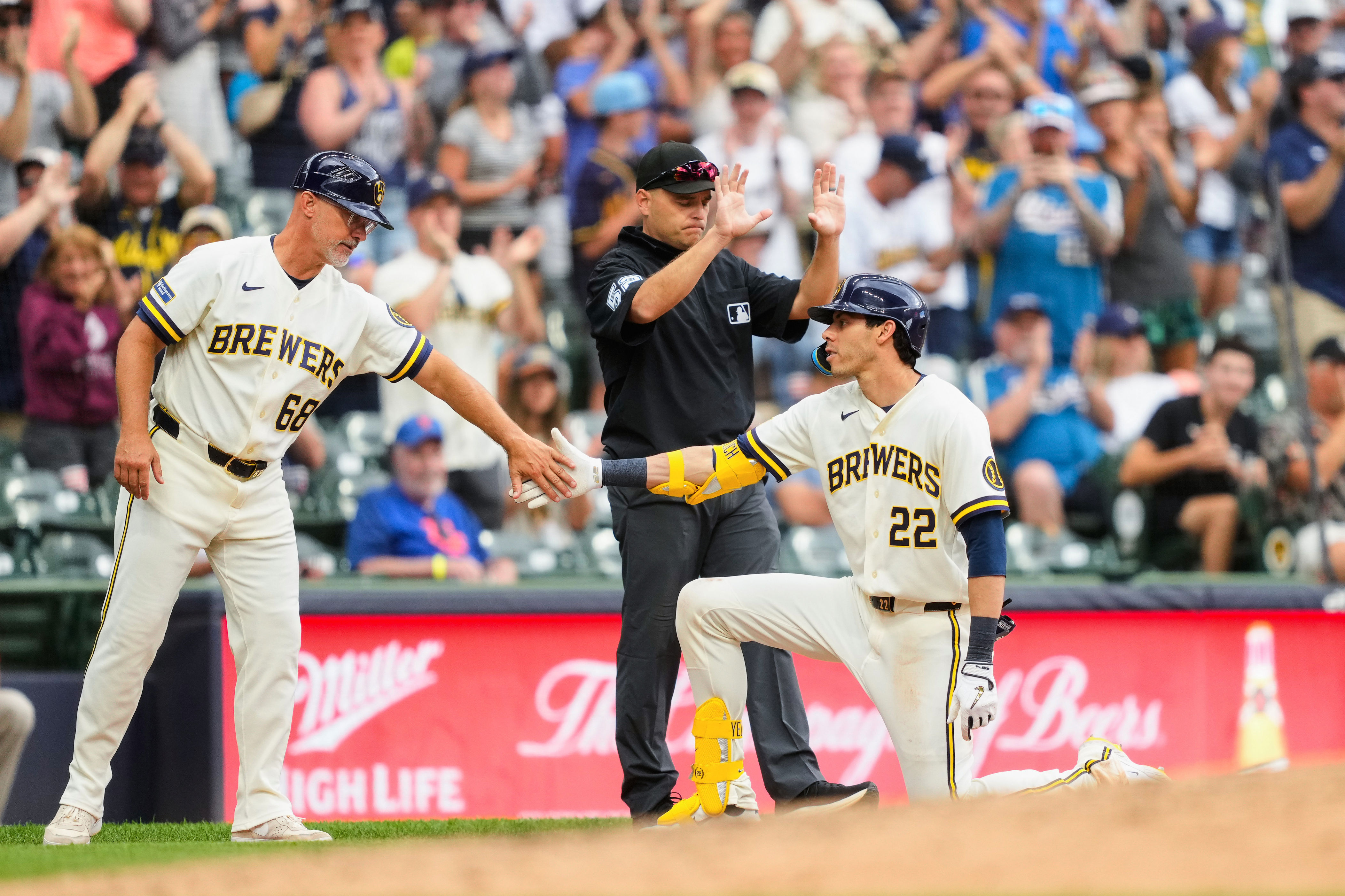 Milwaukee Brewers designated hitter Christian Yelich (22) high-fives third base coach Matt Erickson (68) after hitting an RBI triple as umpire Jansen Visconti (52) looks on during the sixth inning of a baseball game against the New York Mets, Wednesday, July 22, 2026, in Milwaukee. (AP Photo/Kayla Wolf)