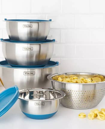 Stacked Viking stainless steel mixing bowls with blue lids next to a stainless steel colander filled with tortellini