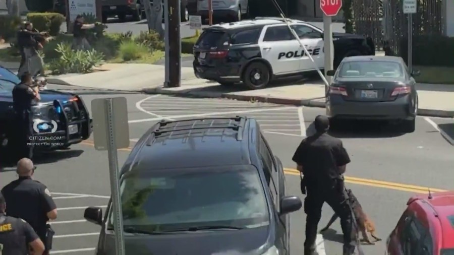 Police officers surround a commercial building as a shirtless man holding a machete is seen during a standoff that ended in an officer-involved shooting