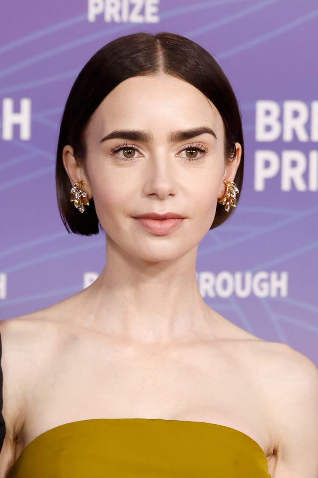 Lily Collins at an event wearing formal attire and earrings with a purple backdrop and the words Breakthrough Prize visible
