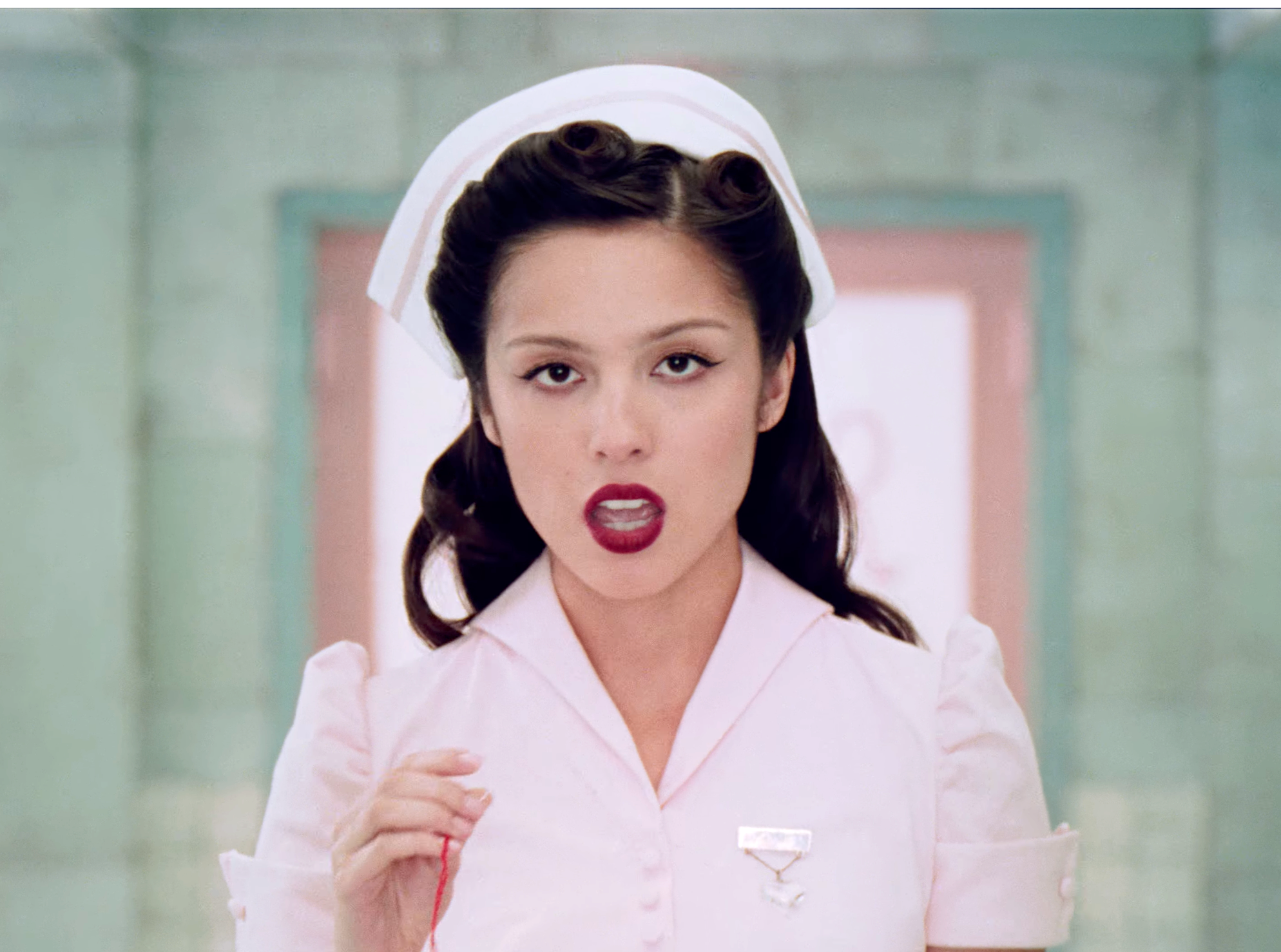 Person dressed as a nurse with vintage hairstyle and makeup, wearing a fitted uniform with a name tag, in a stylized setting.