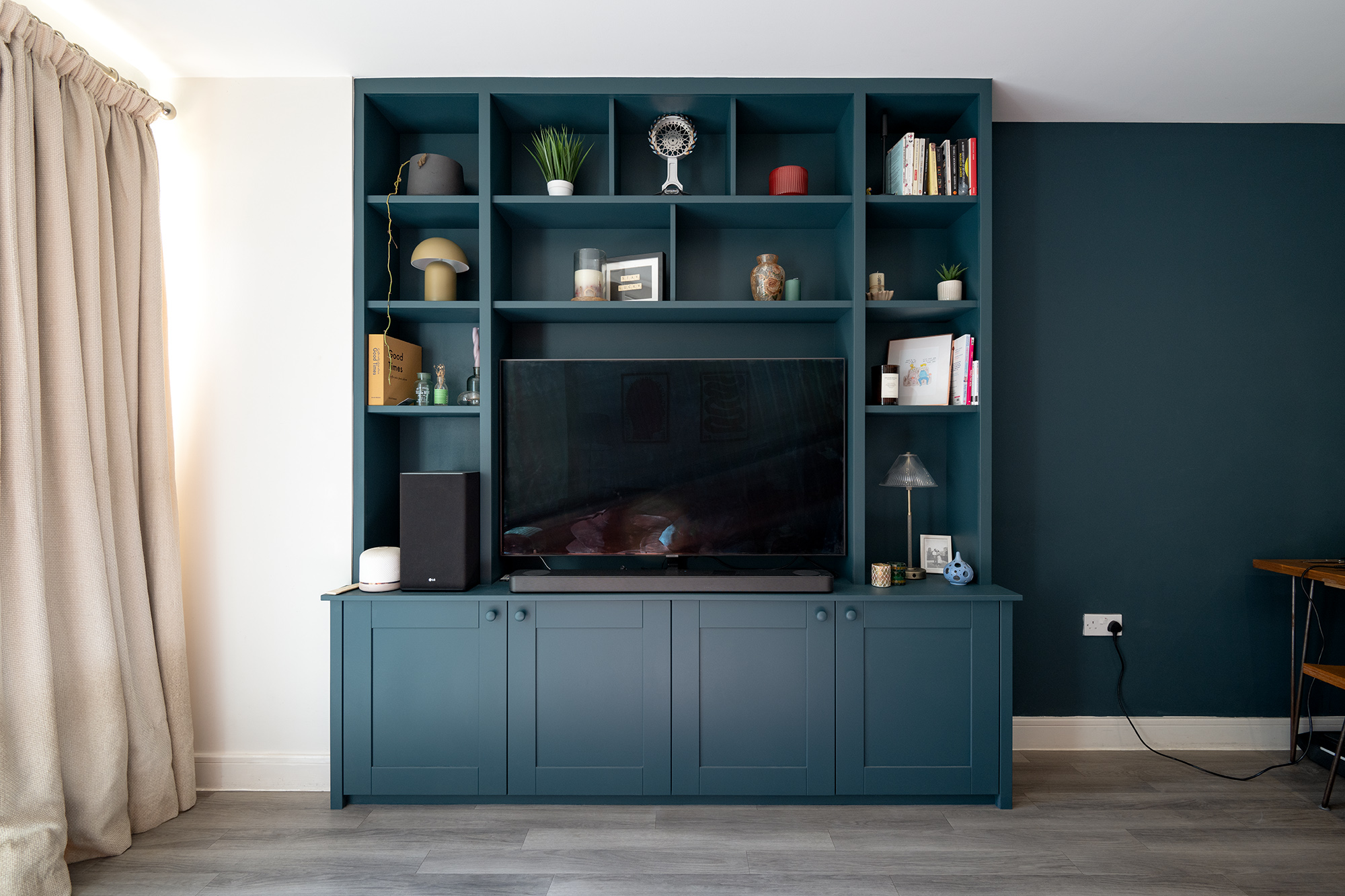 Living room wall painted in navy blue with a bespoke entertainment wall with a TV and shelving