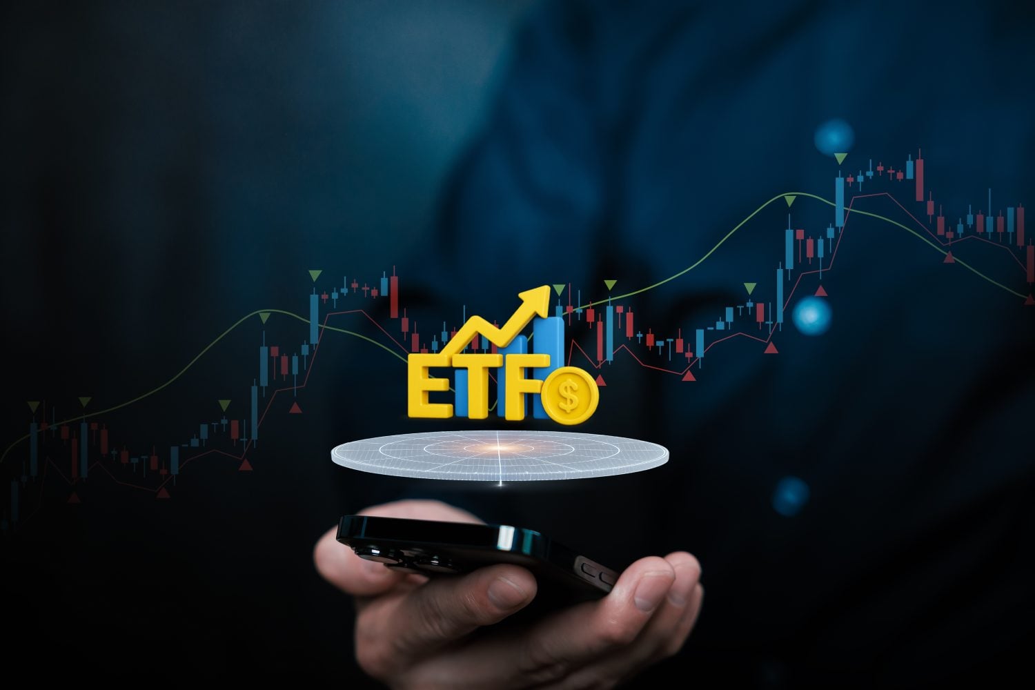 A person's hand holds a black smartphone horizontally. Above the phone, a glowing circular platform projects upward, featuring a yellow 3D text 'ETFO' (where 'O' is a dollar sign coin), a yellow upward-pointing arrow, and blue bar charts. In the dark background, a translucent stock market graph with red and blue candlesticks and curving lines is visible, illuminated by subtle blue lights, suggesting financial data and growth.