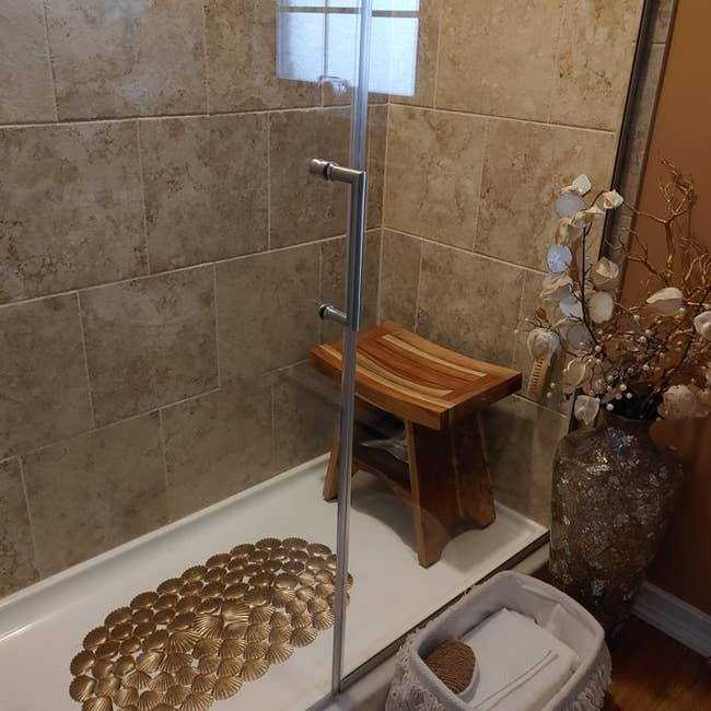 Stylish bathroom with a wooden bench, pebble-style shower mat, and decorative vase. Ideal for a spa-like home setup