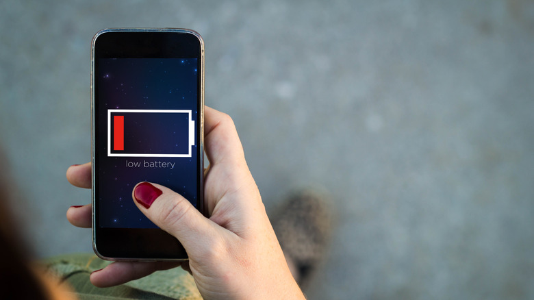 smartphone showing low battery warning sign, hand with dark red fingernails holding it