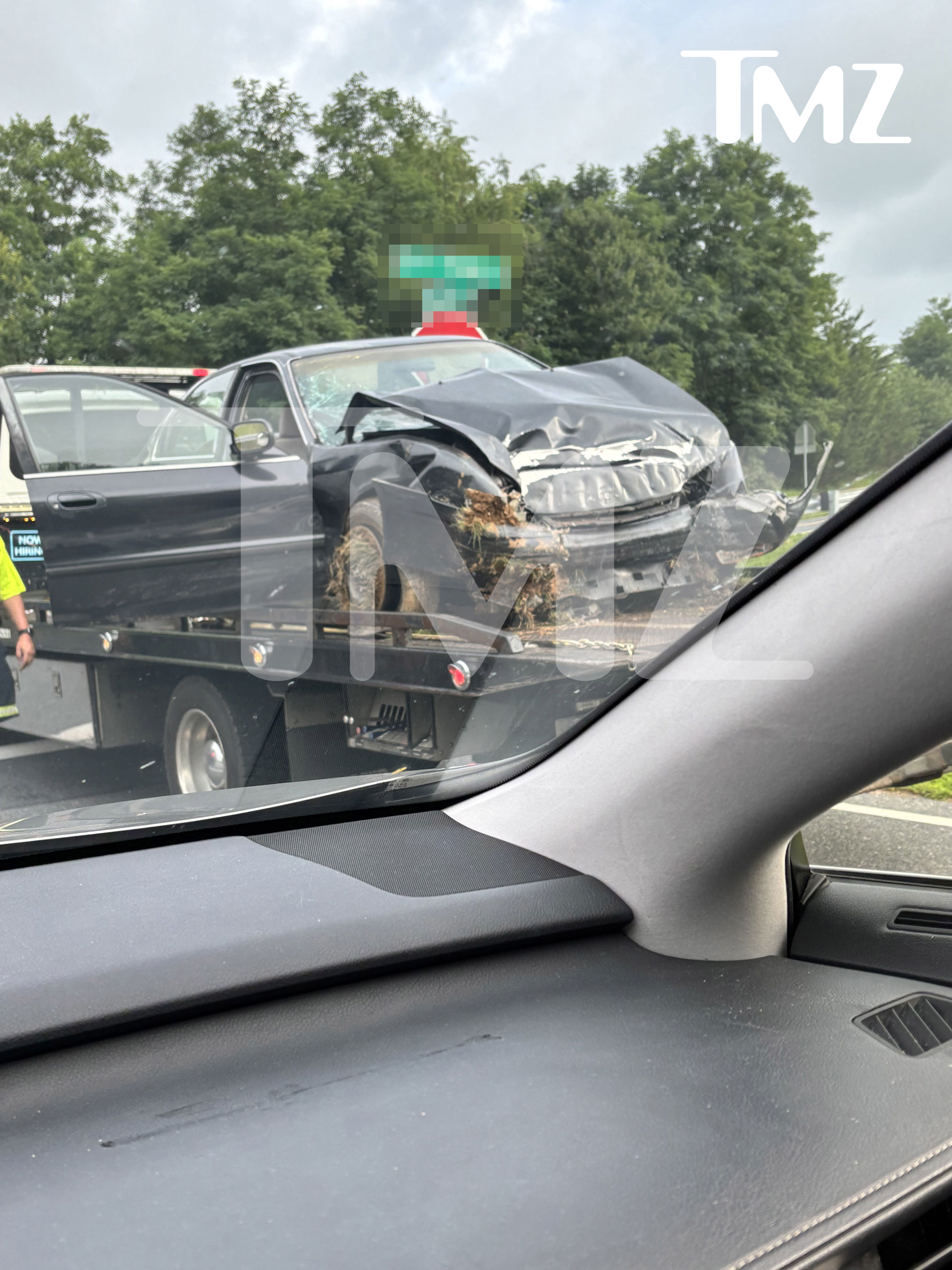 A severely damaged black car, with its front end crushed and windshield shattered, is loaded onto a tow truck.