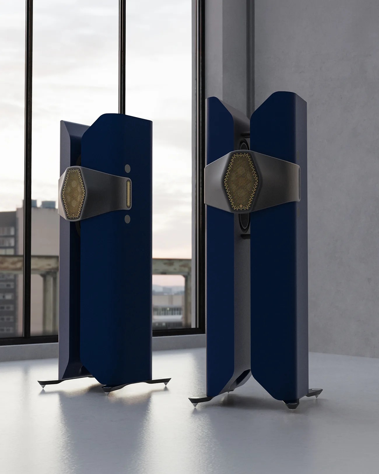Pair of tall, dark blue floor-standing speakers with black and gold mesh accents on a light floor by a window.