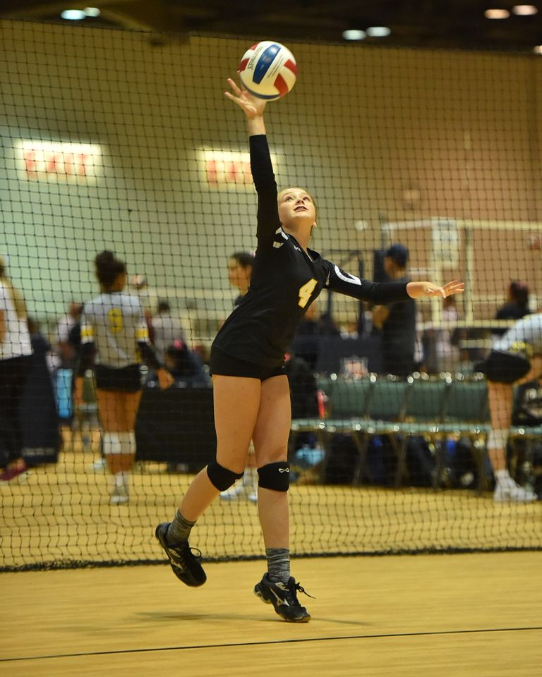 A volleyball player in black athletic attire jumps and hits the ball during a game indoors
